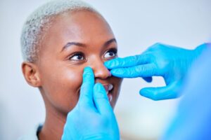 Gloved hands touching patient’s face during rhinoplasty consultation